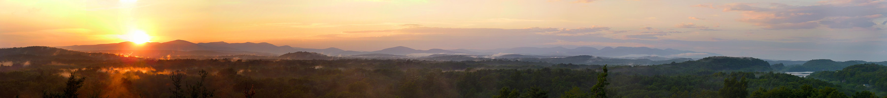 Panoramic shot of a sunset over blue, purple, and black-silhouetted mountains.